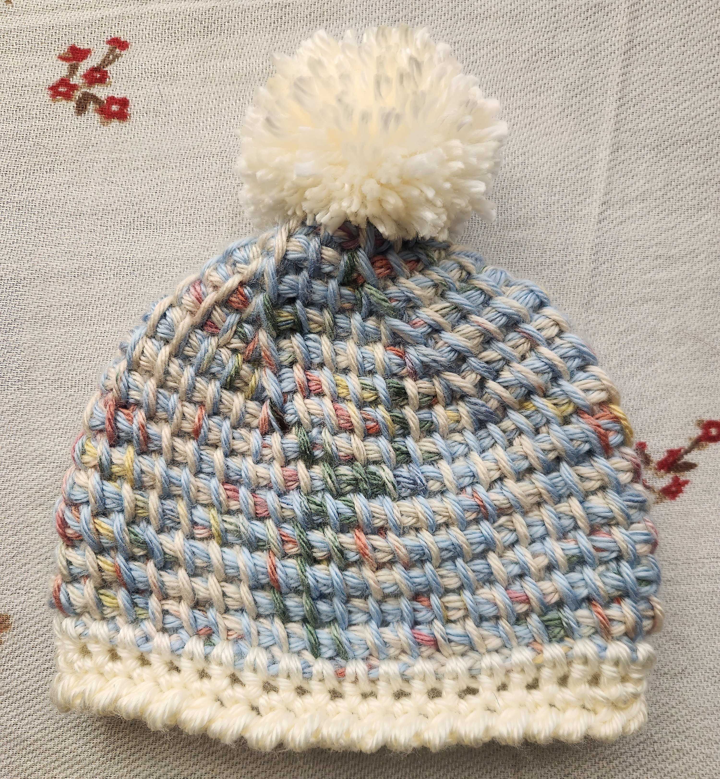 Knit multi-colored hat with a white pom-pom and a white border on the bottom.
