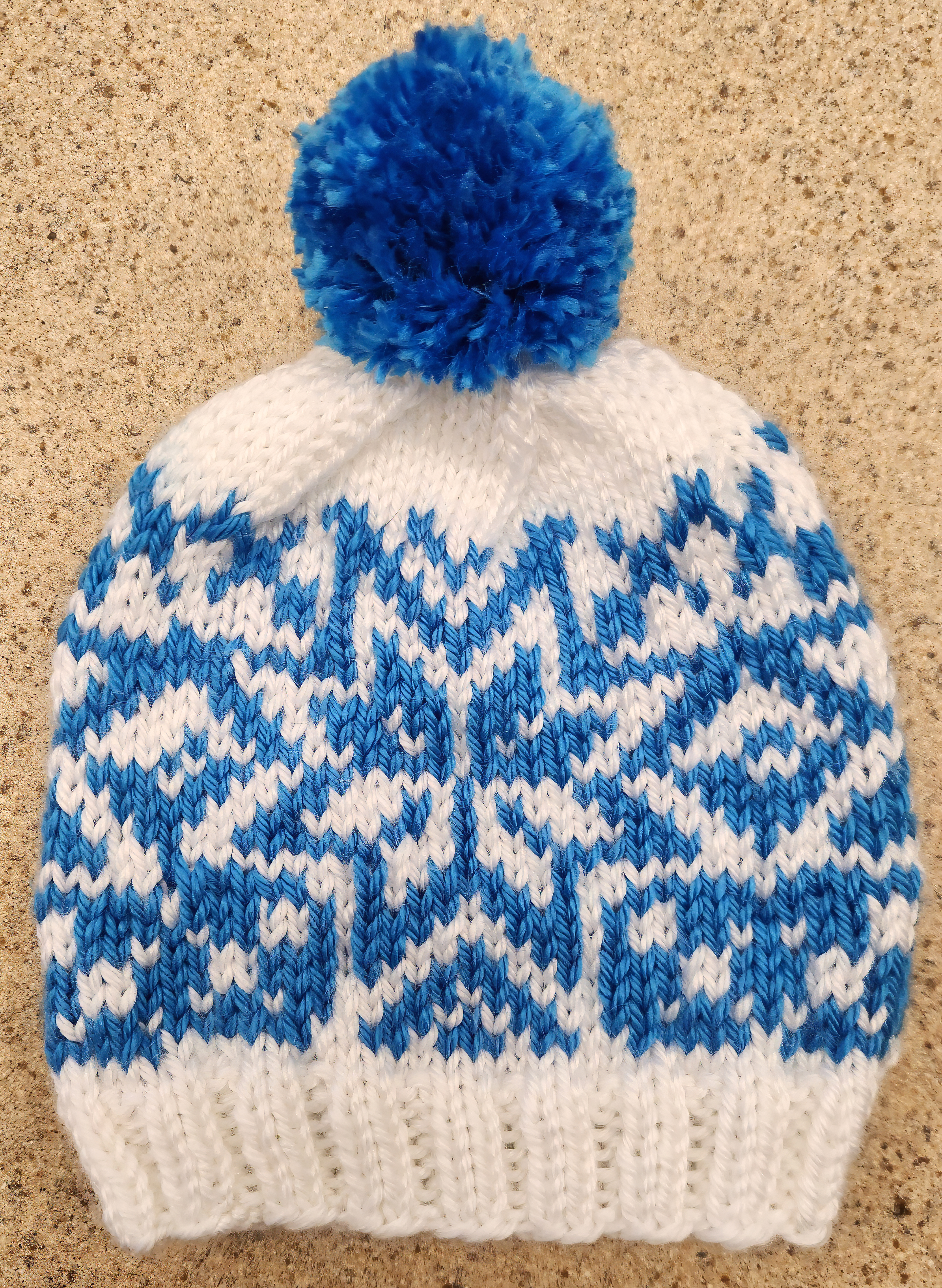 Knit blue and white hat with a blue pom-pom on top and blue snowflake design in the center and going all the way around.