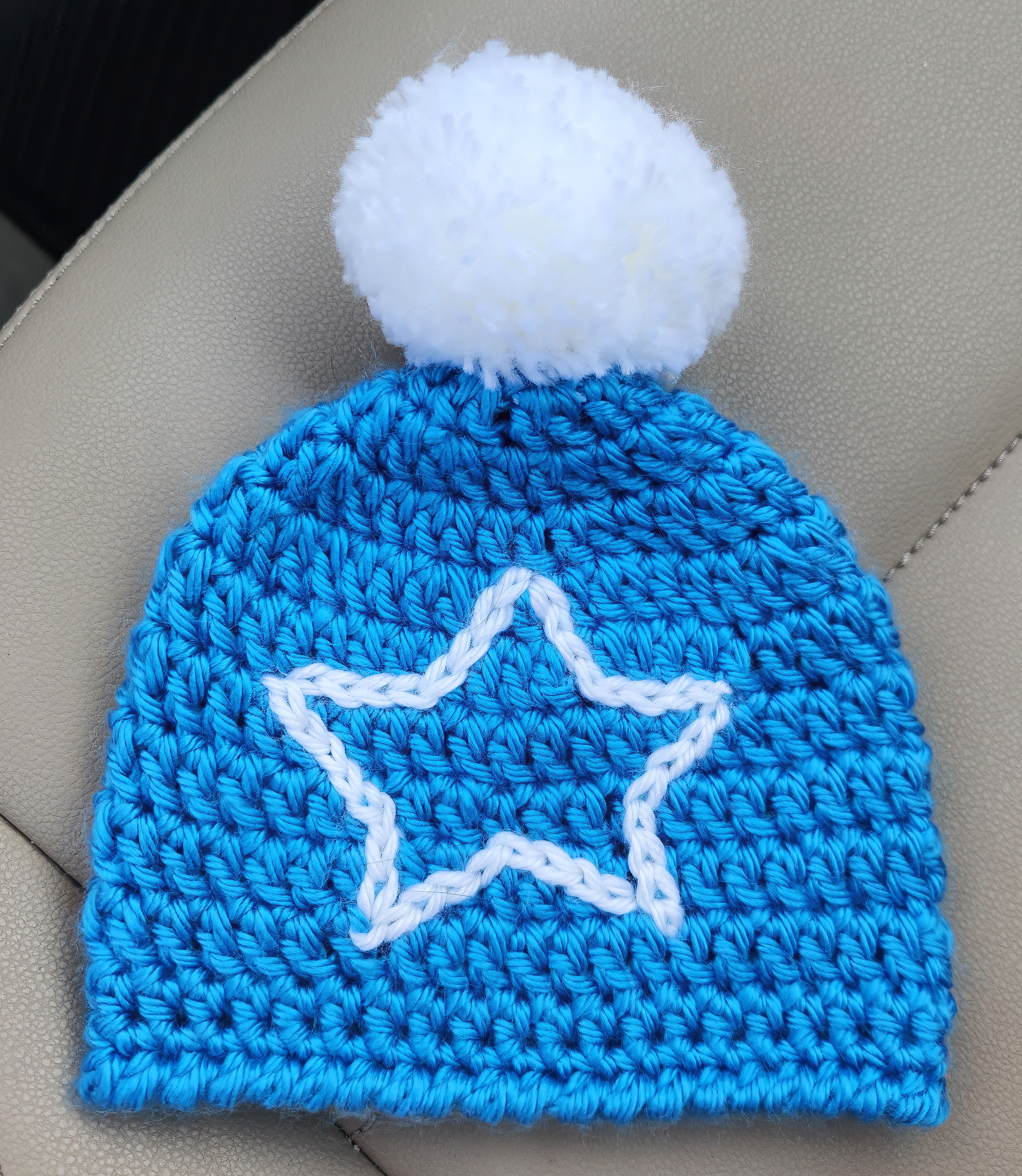 Knit blue hat with a white pom-pom on top and white outline of a star in the center.