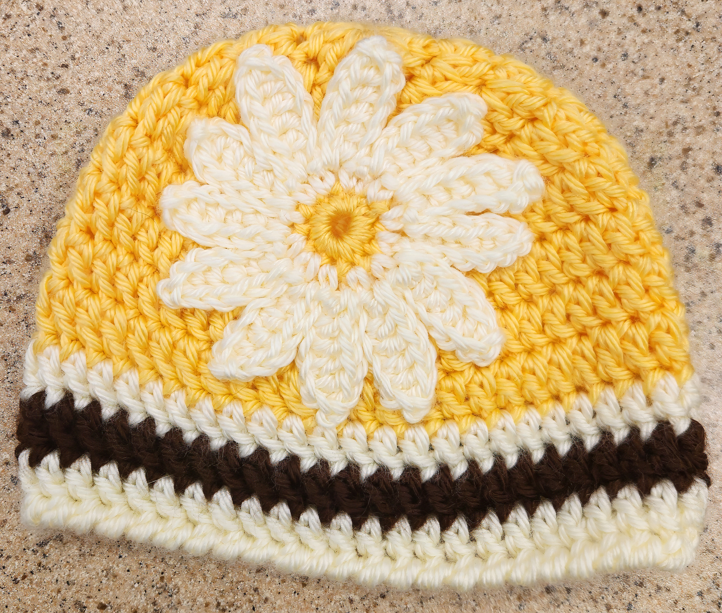 Knit yellow hat with a daisy flower in the center and black-and-white border on the bottom.