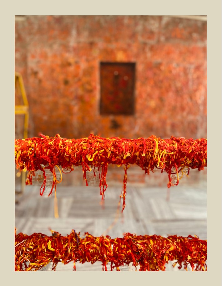 Close-up of two ropes covered in vibrant red and yellow threads, set against a textured, rusty wall.